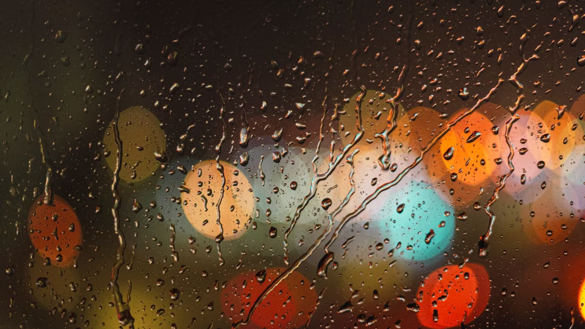 Close-up of raindrops on glass with blurred colorful city lights in the background.